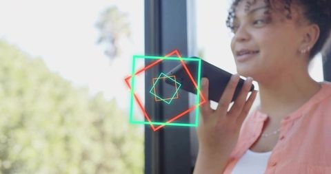 Young woman holding phone and speaking with neon ar geometric overlay by window wearing coral shirt