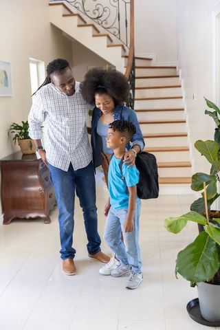 African american parents seeing son off to school in bright home foyer with staircase
