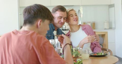 Sunlit modern kitchen family enjoying healthy salad meal together at wooden dining table
