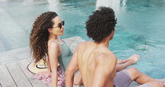 Image of happy diverse couple relaxing in the sun and talking at the poolside of holiday home. Vacation, togetherness, relaxation and inclusivity concept.