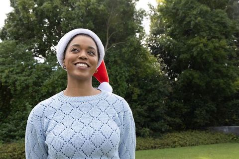 African american woman wearing santa hat smiling outdoors in blue knit sweater, festive
