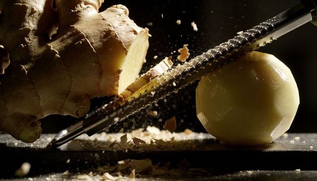 Grating fresh ginger with microplane zester, peeling and rustic shavings closeup