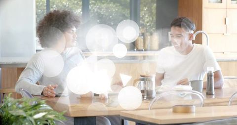 Two friends sharing coffee and laughing at sunlit kitchen table with french press