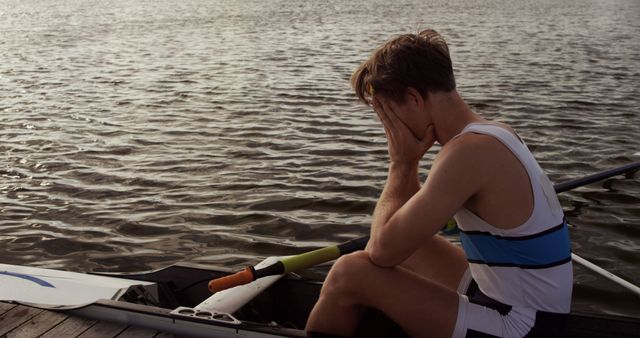 Disappointed caucasian male rower sitting in boat on river with head in hands, copy space. Sport, rowing, hobbies and active lifestyle, unaltered.