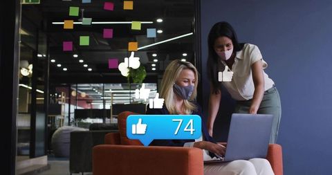 Colleagues collaborating on laptop with social likes overlay in modern office lounge