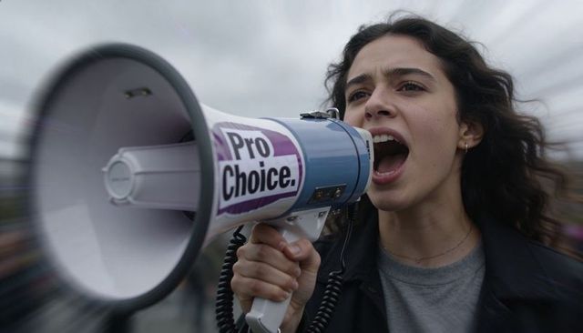 Shouting young woman holding megaphone with pro-choice sticker at women's rights rally