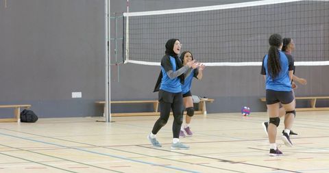 Female volleyball players celebrating point with woman wearing hijab on indoor court