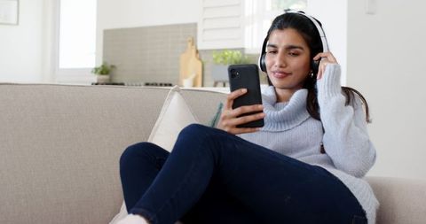 Young Woman Relaxing with Headphones and Smartphone on Cozy Sofa