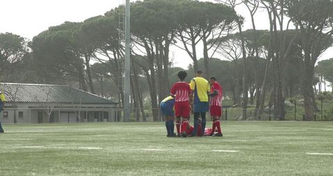 Football team aiding injured teammate on green field