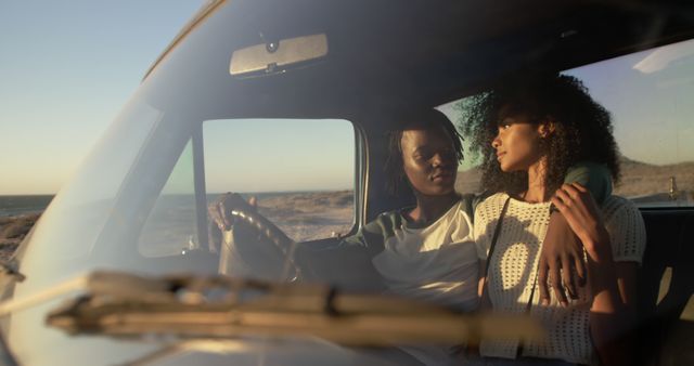 This image shows a young couple in a car driving on a deserted road by the beach during sunset. The serene ambiance and romantic setting are perfect for advertising campaigns related to travel, romance, automobiles, or lifestyle. It can also be used in blog posts or social media to convey themes of adventure, love, and serenity.