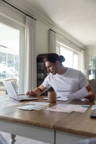 Man working from home at dining table with laptop, color swatches and design papers