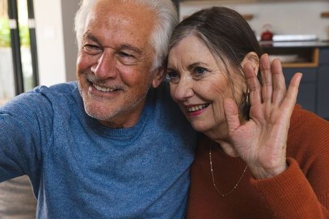 Joyful Senior Couple Relaxing at Home Waving at Camera