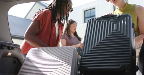 African american women loading hard-shell suitcases into car trunk for road trip