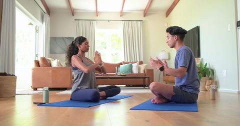 African American couple practicing yoga and meditation on blue mats in sunlit living room
