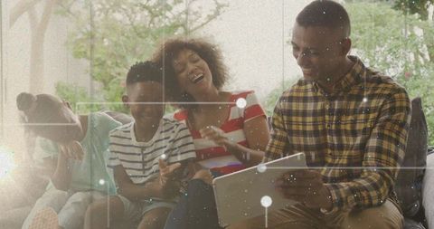 Laughing family on sofa sharing tablet and smartphone, cozy daylight living room moment