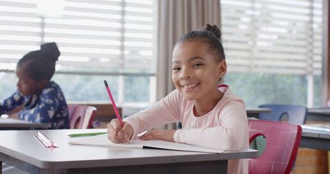 Young Girl Smiling While Writing in Classroom