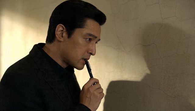 Contemplating asian businessman holding pen against cracked wall casting shadow moody portrait