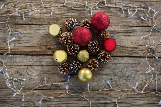 Christmas decorations featuring pine cones and baubles arranged on a wooden background with string lights. Ideal for holiday-themed designs, festive greeting cards, seasonal advertisements, and social media posts celebrating Christmas.