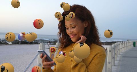 Young woman interacting with emojis on smartphone