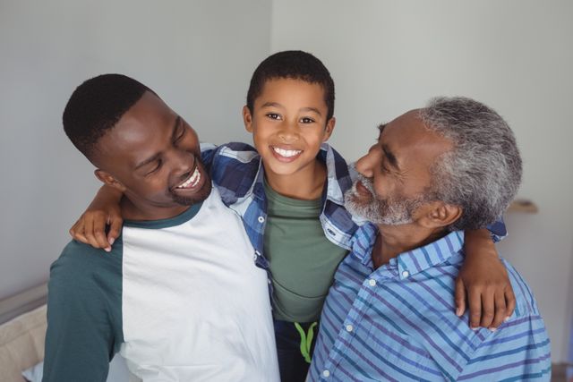 Three generations of an African American family enjoying time together at home. The grandfather, father, and son are smiling and embracing each other, showcasing strong family bonds and happiness. Ideal for use in family-oriented content, advertisements, and articles about parenting, family relationships, and home life.
