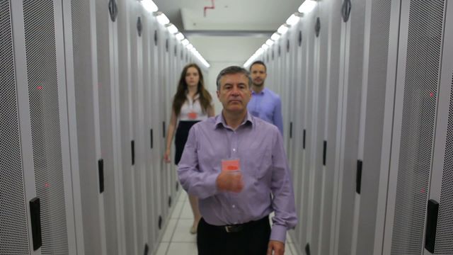 Technicians are walking down a data center hallway filled with server racks, indicating a secure and professional IT environment. Ideal for use in content related to technology, teamwork, network infrastructure, IT management, or cybersecurity. Can be used in marketing materials for tech companies, IT services, data security solutions, or teamwork initiatives.