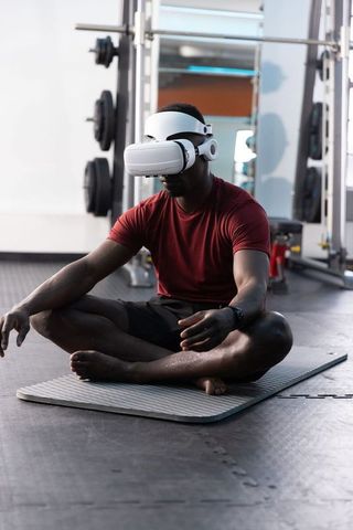 African american man using vr headset meditating on gym mat for virtual fitness