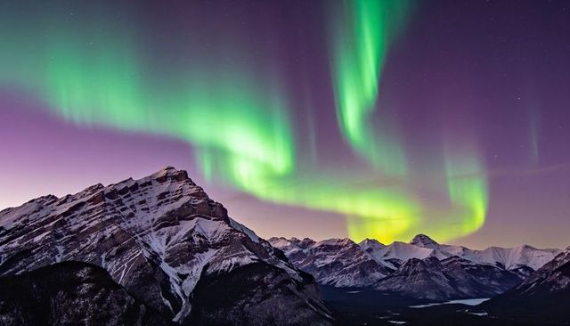 Aurora borealis dancing over jagged snowcapped peaks and frozen river in polar night