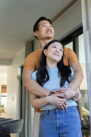 Young couple embracing in sunlit living room looking upward cozy modern home romance