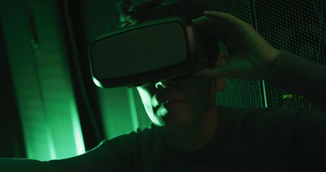 Man exploring virtual reality with VR headset in dimly lit green environment. Could be used for tech blogs, VR product advertising, gaming promotions, futuristic themes or articles on digital transformation.