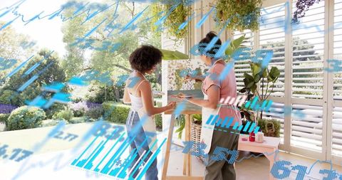 Two women painting on sunroom porch, mixing paints and collaborating with garden view