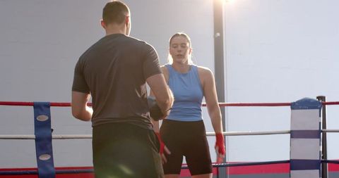 Trainer Holding Focus Mitts While Female Boxer Pausing in Sunlit Boxing Ring