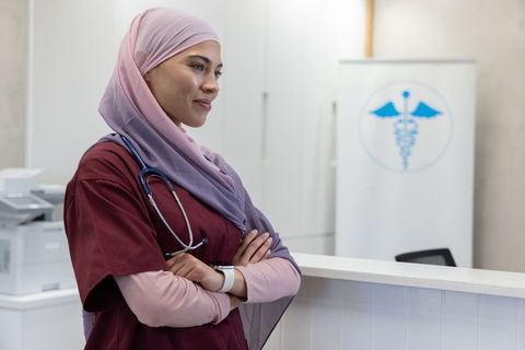 African american nurse standing at clinic reception wearing hijab stethoscope smartwatch