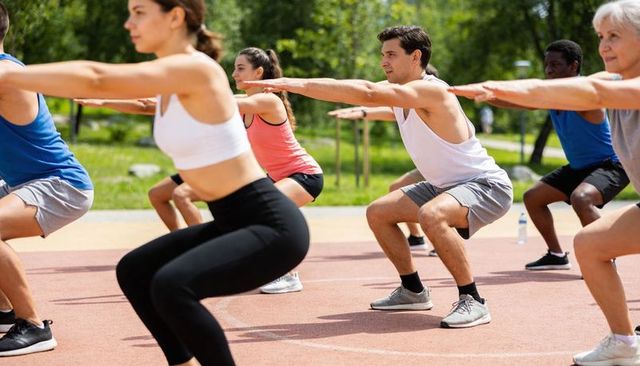 Diverse group performing squats on outdoor track in park for group fitness training