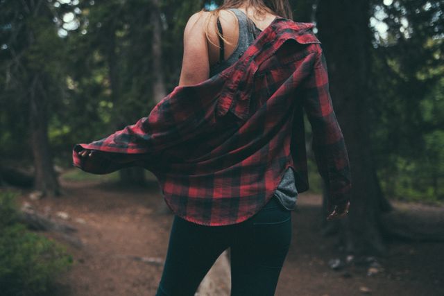 Woman walking in forest trail wearing plaid shirt and jeans, symbolizing freedom and connection with nature. Perfect for themes on outdoor adventures, casual fashion, exploring nature, and leisure activities.