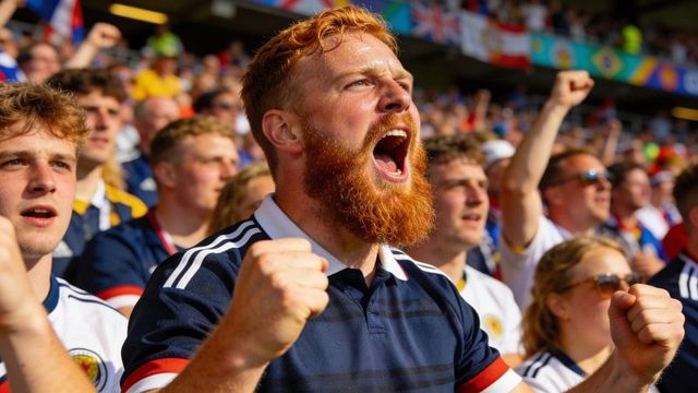 Red-bearded fan cheering and clenching fists in football crowd