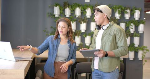 Coworkers pointing at laptop and collaborating with tablet in modern coworking space