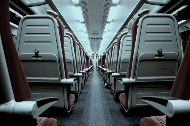 Empty train interior showing symmetrical rows of reserved seats. Ideal for travel agency ads, blog posts about public transportation, commuting, urban travel stories, magazines focusing on modern infrastructure, and educational materials about rail travel.