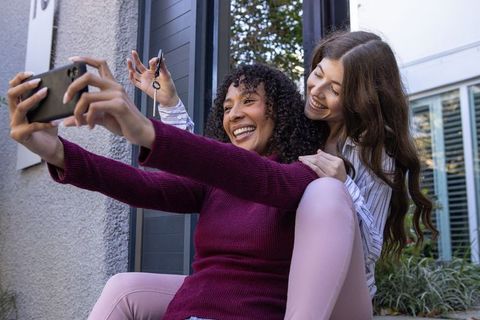 Joyful diverse female friends taking selfie with new house key