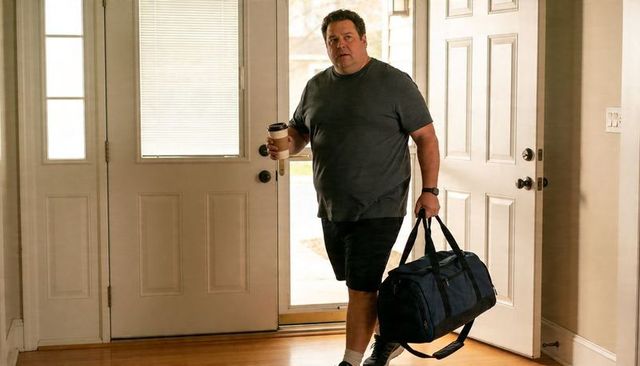 Man entering home carrying navy duffel bag and coffee cup morning arrival travel lifestyle