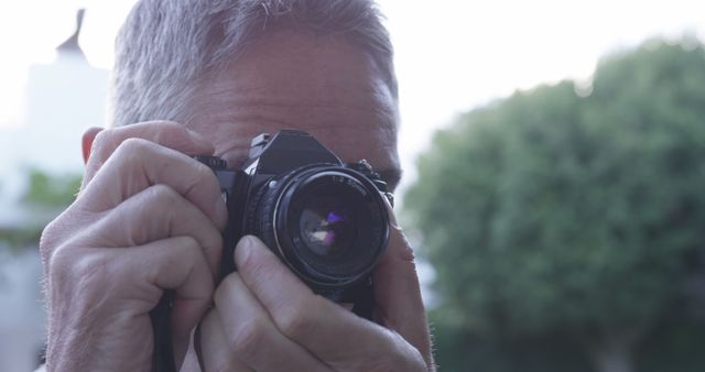 Close-up view of a man using a vintage camera to take photos outdoors. Ideal for themes related to photography, hobbies, vintage cameras, or outdoor photography activities.
