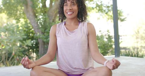 African american woman meditating on covered patio wearing fitness watch, yoga wellness lifestyle