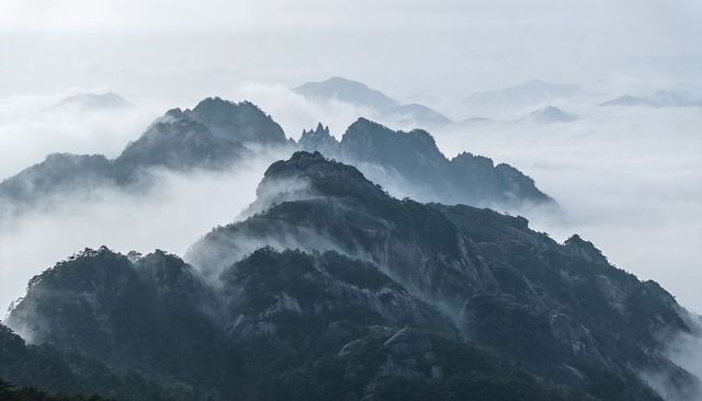 Misty mountain ridges and granite peaks rising through sea of fog, serene alpine panorama
