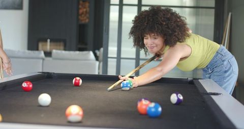 African american woman lining up pool shot on black-felt table in modern living room