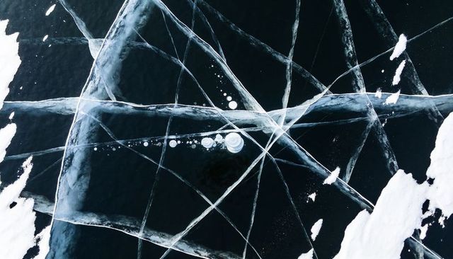 Revealing aerial cracked black ice showing intersecting fractures and trapped bubbles