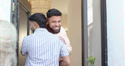 Friends embracing at front doorway greeting with warm smiles and casual summer clothing