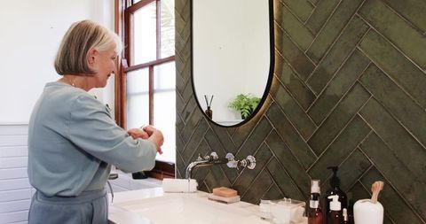 Senior woman washing hands in modern bathroom for hygienic routine
