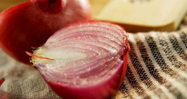 Red onion half, freshly sliced, sitting on striped kitchen towel. Clear layers and droplets of water can be seen. Ideal for use in cooking blogs, healthy eating promotions, recipe ingredients, and food presentations.