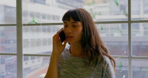 Woman speaking on smartphone by urban grid window with green stickers, casual lifestyle