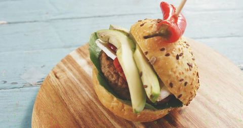 Seeded avocado burger with grilled patty and chili pepper skewer on rustic cutting board
