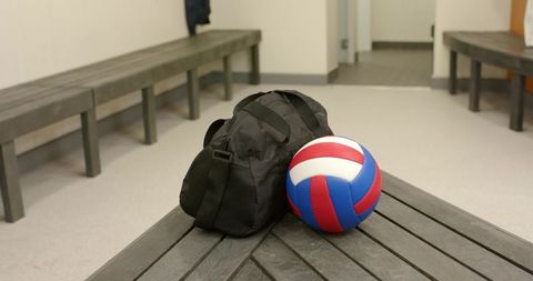 Volleyball duffel and red-white-blue ball sitting on slatted bench in locker room